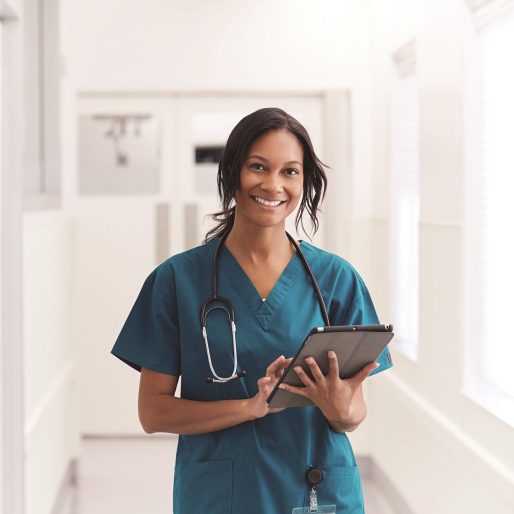 Portrait Of Smiling Female Doctor Wearing Scrubs In Hospital Corridor Holding Digital Tablet